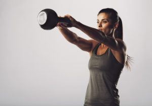 Image of young attractive female doing kettle bell exercise on grey background. Fitness woman working out. Crossfit exercise.