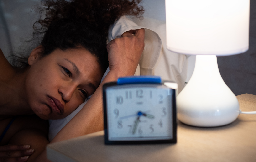 Woman In Bed Looking at Alarm Clock